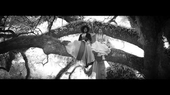 Movie still from “Lemonade” (2016), directed by Mark Romanek – Two women sitting on a tree branch in front of a sky background; Wide shot, Low angle