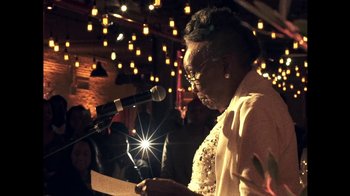 Movie still from “Lemonade” (2016), directed by Mark Romanek – An older woman is speaking into a microphone at an event; Close Up shot, Low angle