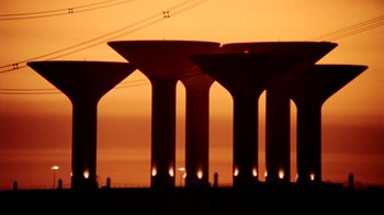 Movie still from “Lessons of Darkness” (1992), directed by Werner Herzog – A view of a bunch of water towers at sunset; Extreme Wide shot, Low angle