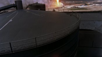 Movie still from “Lessons of Darkness” (1992), directed by Werner Herzog – An oil storage tank is shown with smoke billowing from it in the background; Extreme Wide shot, High angle