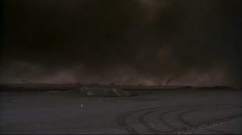 Movie still from “Lessons of Darkness” (1992), directed by Werner Herzog – A person standing in the middle of an empty field at night; Extreme Wide shot, High angle
