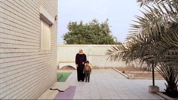 Movie still from “Lessons of Darkness” (1992), directed by Werner Herzog – An older woman and a young boy walking on a sidewalk; Wide shot, Low angle
