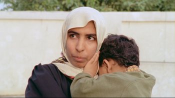 Movie still from “Lessons of Darkness” (1992), directed by Werner Herzog – A woman wearing a headscarf is holding a child; Close Up shot, High angle