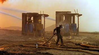 Movie still from “Lessons of Darkness” (1992), directed by Werner Herzog – A man is spraying water from a fire hose; Extreme Wide shot, Low angle