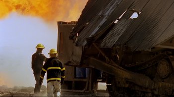 Movie still from “Lessons of Darkness” (1992), directed by Werner Herzog – Two firemen are standing next to a destroyed building; Wide shot, Low angle