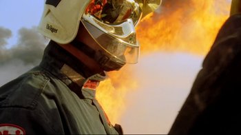 Movie still from “Lessons of Darkness” (1992), directed by Werner Herzog – A person wearing a helmet with a fire in the background; Extreme Close Up shot, Low angle