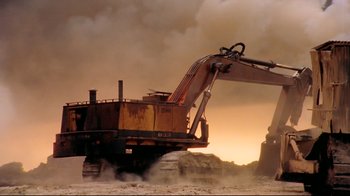 Movie still from “Lessons of Darkness” (1992), directed by Werner Herzog – An excavator is in the dirt with smoke billowing from it; Extreme Wide shot, Low angle