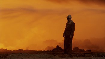 Movie still from “Lessons of Darkness” (1992), directed by Werner Herzog – A man standing on top of a dirt field; Wide shot, Low angle