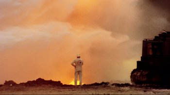 Movie still from “Lessons of Darkness” (1992), directed by Werner Herzog – A man standing in front of a fire in the desert; Extreme Wide shot, Low angle