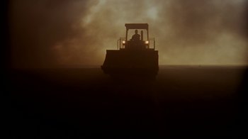 Movie still from “Lessons of Darkness” (1992), directed by Werner Herzog – A man riding a tractor on top of a field; Extreme Wide shot, Low angle