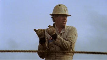 Movie still from “Lessons of Darkness” (1992), directed by Werner Herzog – A man wearing a hard hat and gloves is holding something; Medium shot, Low angle