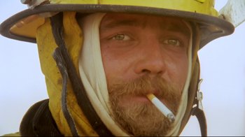Movie still from “Lessons of Darkness” (1992), directed by Werner Herzog – A person wearing a helmet smoking a cigarette; Close Up shot, High angle