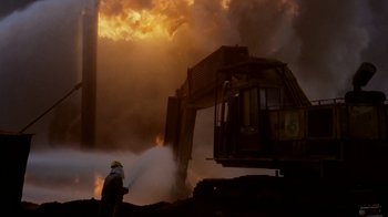 Movie still from “Lessons of Darkness” (1992), directed by Werner Herzog – A fire fighter spraying water on a fire truck; Extreme Wide shot, Low angle
