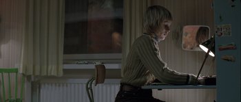 Movie still from “Let the Right One In” (2008), directed by Tomas Alfredson – A person sitting at a table with a laptop; Medium shot, Low angle