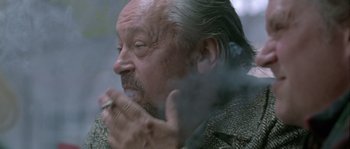 Movie still from “Let the Right One In” (2008), directed by Tomas Alfredson – An older man smoking a cigarette while wearing a jacket; Close Up shot, Low angle