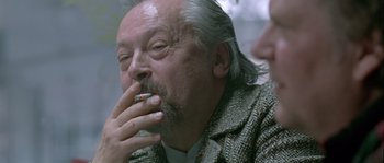 Movie still from “Let the Right One In” (2008), directed by Tomas Alfredson – An older man smoking a cigarette while sitting down; Close Up shot, Over the shoulder angle