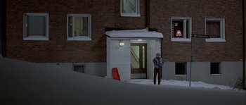 Movie still from “Let the Right One In” (2008), directed by Tomas Alfredson – A man standing in front of a building in the snow; Wide shot, High angle