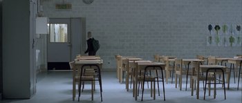 Movie still from “Let the Right One In” (2008), directed by Tomas Alfredson – A person walking in front of some tables and chairs in a room; Wide shot, High angle