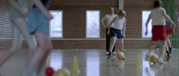 Movie still from “Let the Right One In” (2008), directed by Tomas Alfredson – A man and a woman kicking a ball in a gym; Wide shot, Over the shoulder angle