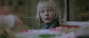 Movie still from “Let the Right One In” (2008), directed by Tomas Alfredson – A young girl sitting at a table looking at the camera; Close Up shot, Over the shoulder angle