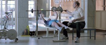 Movie still from “Let the Right One In” (2008), directed by Tomas Alfredson – A man and a woman are working out in a gym; Medium shot, Over the shoulder angle
