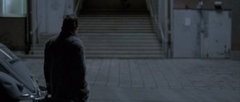 Movie still from “Let the Right One In” (2008), directed by Tomas Alfredson – A person walking down a sidewalk near a set of stairs; Wide shot, Over the shoulder angle