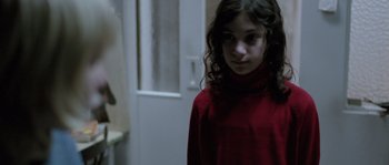Movie still from “Let the Right One In” (2008), directed by Tomas Alfredson – A young girl in a red shirt standing in front of a door; Close Up shot, Over the shoulder angle