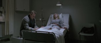 Movie still from “Let the Right One In” (2008), directed by Tomas Alfredson – A woman lying in a hospital bed while a man looks on; Medium shot, Low angle