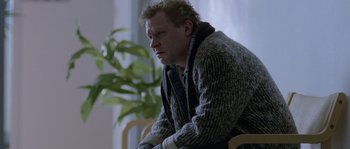 Movie still from “Let the Right One In” (2008), directed by Tomas Alfredson – A man sitting on a chair in a living room; Medium shot, Low angle