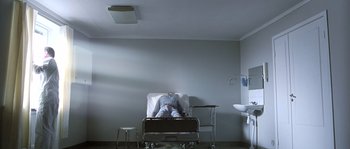 Movie still from “Let the Right One In” (2008), directed by Tomas Alfredson – A man sitting in a hospital bed in a room; Wide shot, High angle