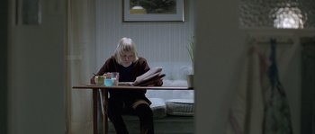 Movie still from “Let the Right One In” (2008), directed by Tomas Alfredson – A woman sitting at a table reading a magazine; Medium shot, High angle