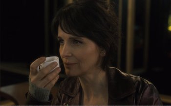 Movie still from “Let the Sunshine In” (2017), directed by Claire Denis – A woman is holding a cell phone up to her mouth; Close Up shot, Over the shoulder angle