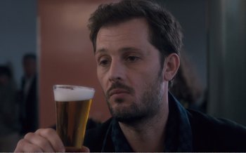 Movie still from “Let the Sunshine In” (2017), directed by Claire Denis – A person holding a glass of beer; Close Up shot, Over the shoulder angle