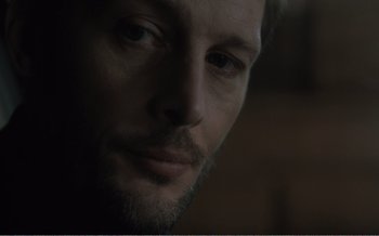 Movie still from “Let the Sunshine In” (2017), directed by Claire Denis – A man with a beard looking at the camera; Close Up shot, Low angle