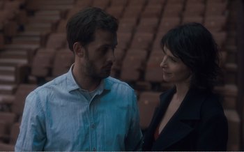 Movie still from “Let the Sunshine In” (2017), directed by Claire Denis – A man and a woman standing next to each other in front of an audience; Medium shot, Over the shoulder angle
