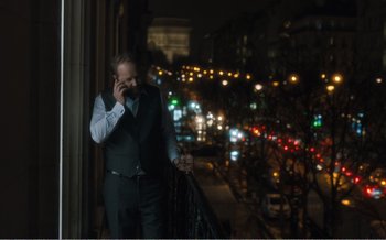 Movie still from “Let the Sunshine In” (2017), directed by Claire Denis – A man standing on a balcony talking on a cell phone; Medium shot, Over the shoulder angle
