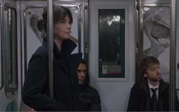 Movie still from “Let the Sunshine In” (2017), directed by Claire Denis – A woman standing next to a man on a subway train; Medium shot, Over the shoulder angle