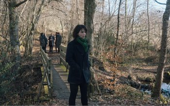 Movie still from “Let the Sunshine In” (2017), directed by Claire Denis – A woman standing on a bridge in the woods; Wide shot, Over the shoulder angle