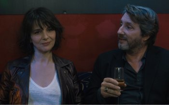 Movie still from “Let the Sunshine In” (2017), directed by Claire Denis – A man and a woman sitting next to each other holding wine glasses; Close Up shot, Over the shoulder angle