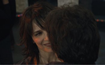 Movie still from “Let the Sunshine In” (2017), directed by Claire Denis – A woman smiles at another woman in front of a building; Close Up shot, Over the shoulder angle