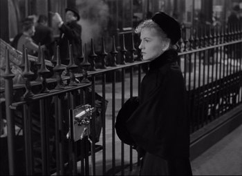 Movie still from “Letter from an Unknown Woman” (1948), directed by Max Ophüls – A black and white photo of a woman standing next to an iron fence; Medium shot, Low angle
