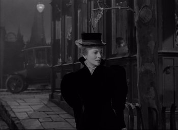 Movie still from “Letter from an Unknown Woman” (1948), directed by Max Ophüls – A woman wearing a top hat standing in front of a building; Medium shot, Over the shoulder angle