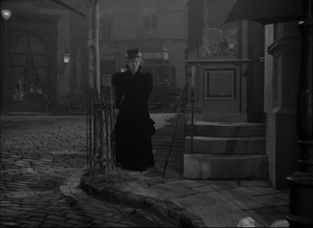 Movie still from “Letter from an Unknown Woman” (1948), directed by Max Ophüls – An old photo of a man in a black coat and a hat; Wide shot, High angle
