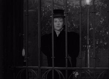 Movie still from “Letter from an Unknown Woman” (1948), directed by Max Ophüls – A woman wearing a top hat standing behind a fence; Medium shot, Low angle