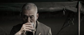 Movie still from “Letters from Iwo Jima” (2006), directed by Clint Eastwood – A man in a suit drinking from a cup; Close Up shot, Over the shoulder angle