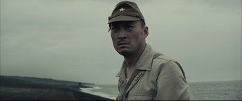 Movie still from “Letters from Iwo Jima” (2006), directed by Clint Eastwood – A man in a military uniform standing in front of a body of water; Close Up shot, Low angle
