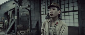 Movie still from “Letters from Iwo Jima” (2006), directed by Clint Eastwood – A man wearing a hat is standing in front of a building; Medium shot, Low angle