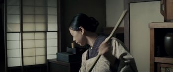 Movie still from “Letters from Iwo Jima” (2006), directed by Clint Eastwood – A woman holding a wooden stick in a room; Medium shot, Low angle