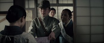 Movie still from “Letters from Iwo Jima” (2006), directed by Clint Eastwood – A man in a hat is holding a ticket; Medium shot, Over the shoulder angle