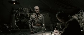 Movie still from “Letters from Iwo Jima” (2006), directed by Clint Eastwood – A man in a military uniform standing in front of a table; Medium shot, Over the shoulder angle